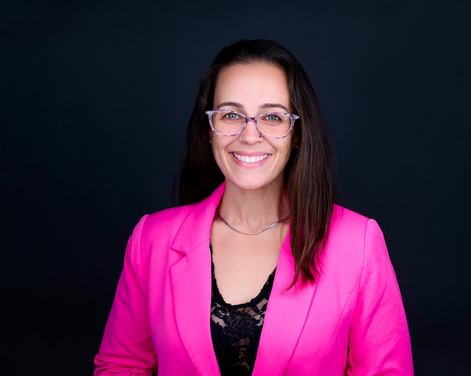 Marla Osner, CRNP, founder of Eclipse Total Health, smiling in a bright pink blazer against a near-black studio background